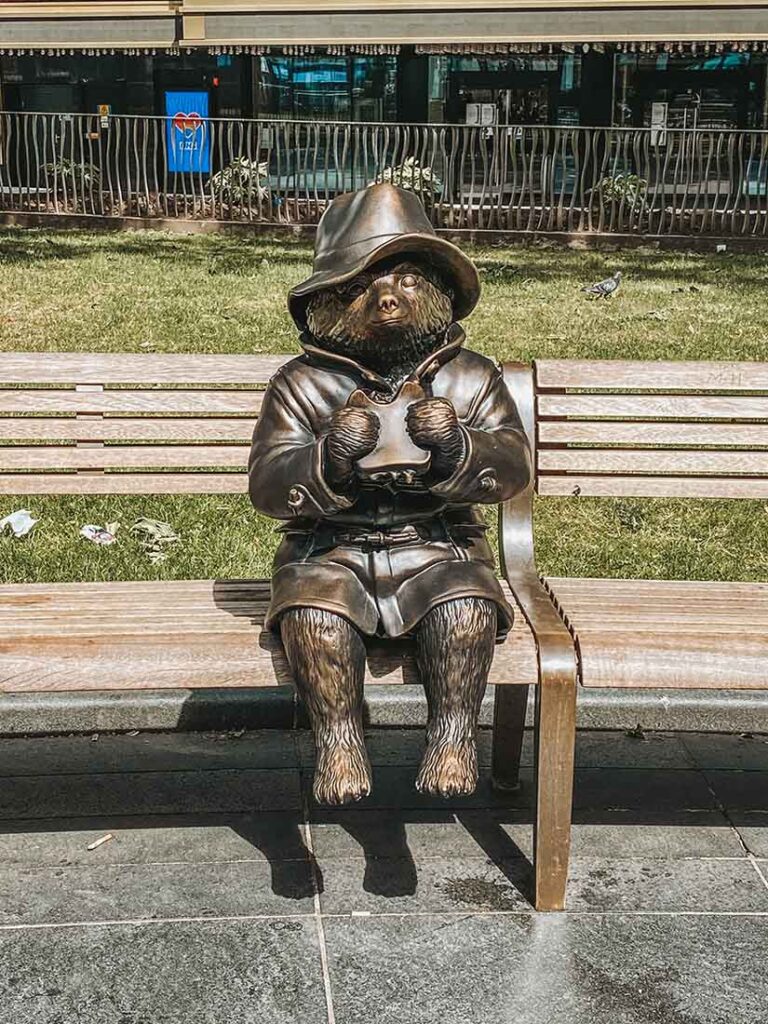  bronze statue of Paddington Bear sitting on bench eating his sandwiches in Leicester Square London 