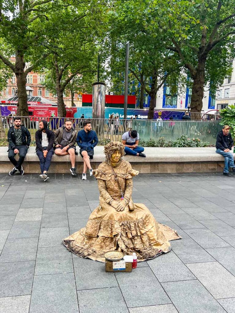 Golden lady statue performer in londons Leicester Square dressed in gold dress with tip pot in front