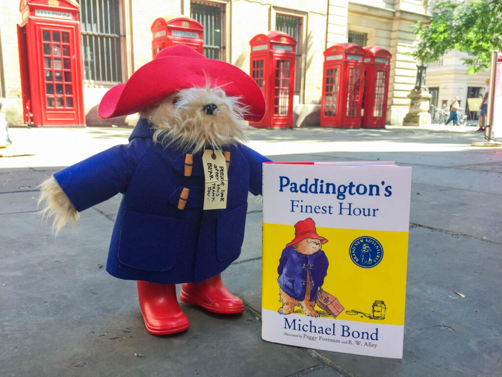 Paddington Bear toy and his book outside red phone boxes in London